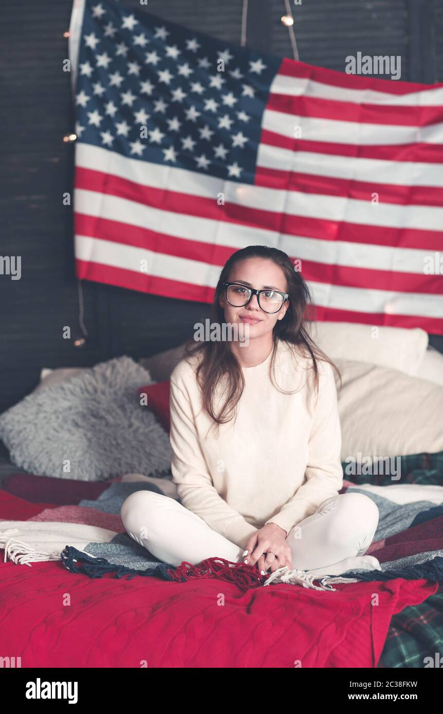 Jolie femme en tenue décontractée sur le lit avec drapeau américain sur le mur Banque D'Images