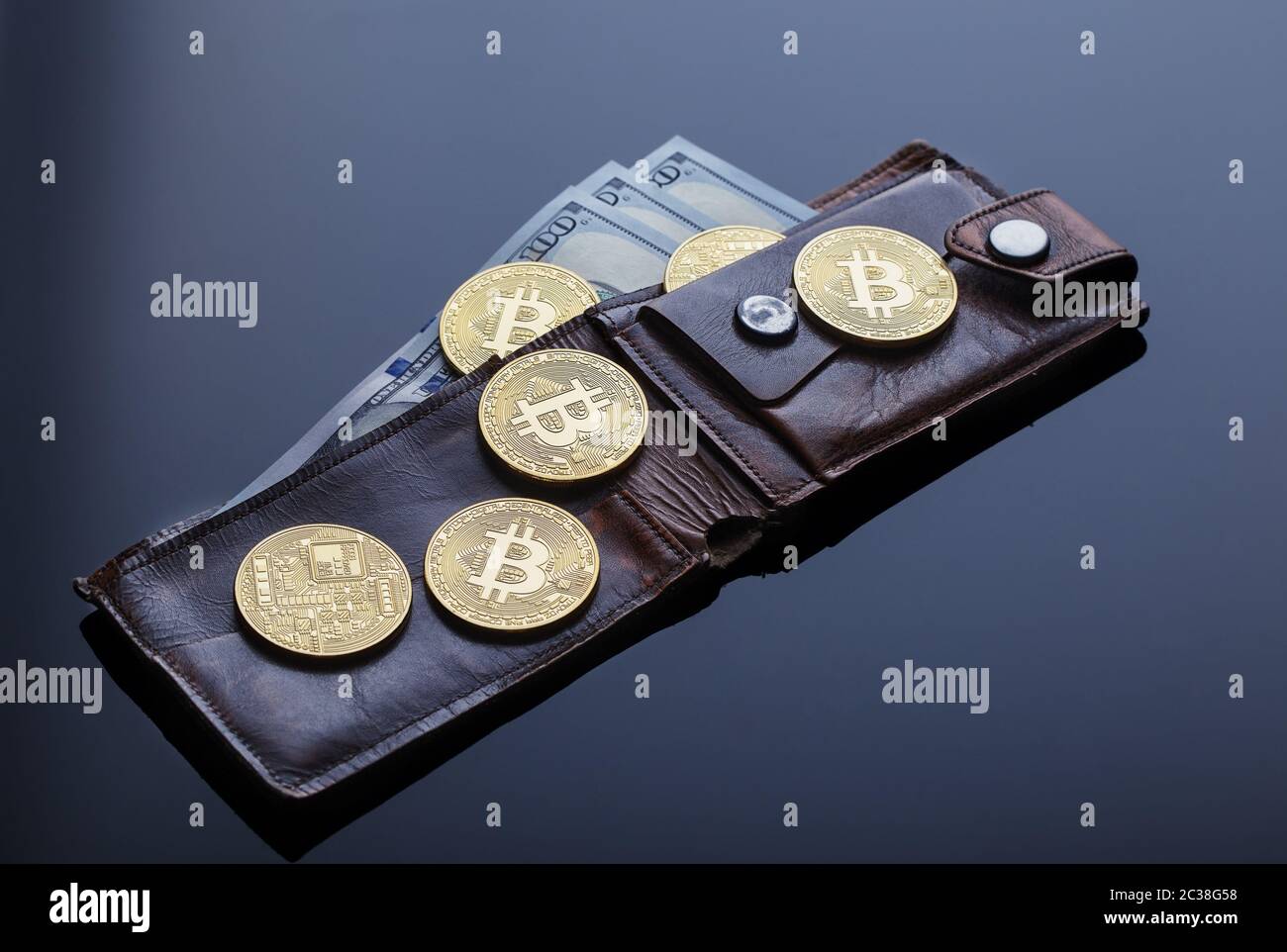 Portefeuille avec bitcoins d'or et billets de cent dollars sur fond sombre. Le concept de l'activité virtuelle et de la monnaie. Banque D'Images