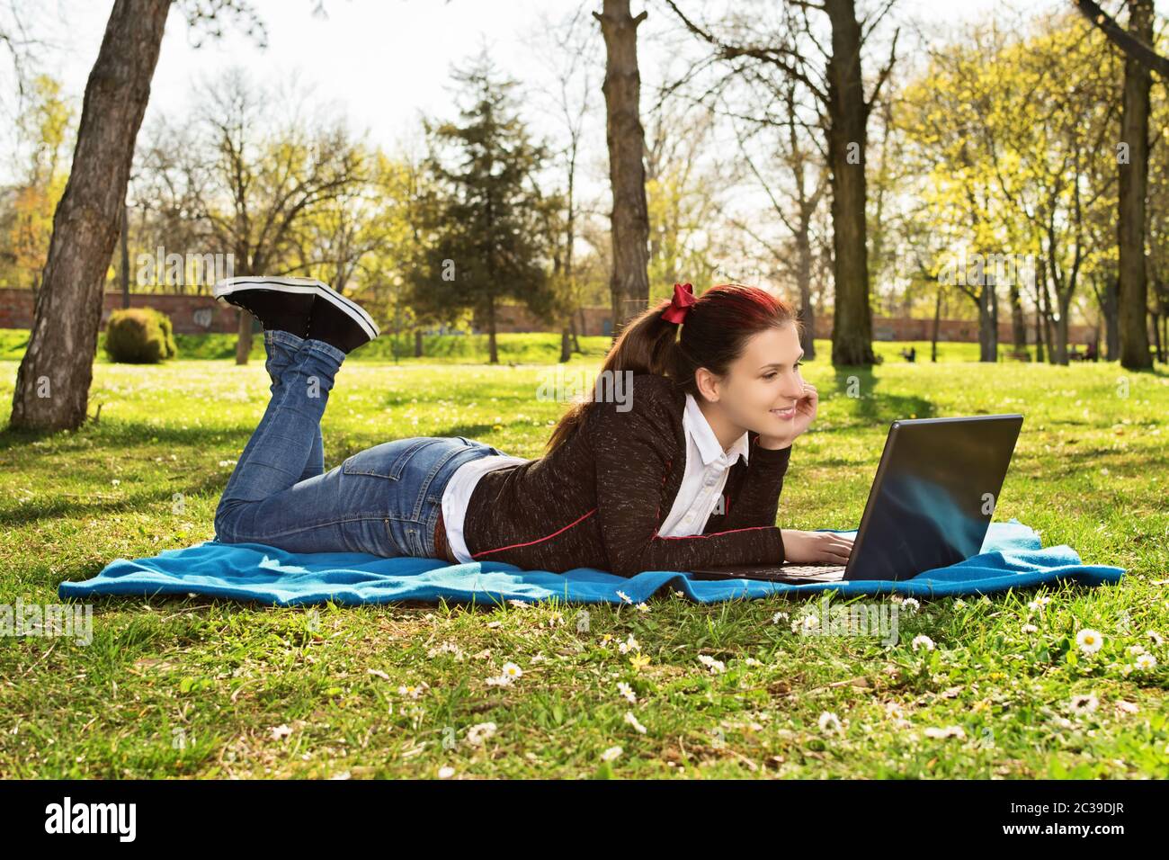 Belle fille étudiante décontractée avec ordinateur portable à l'extérieur. Femme souriante couchée sur une couverture sur l'herbe avec ordinateur, surfer sur Internet ou préparer Banque D'Images