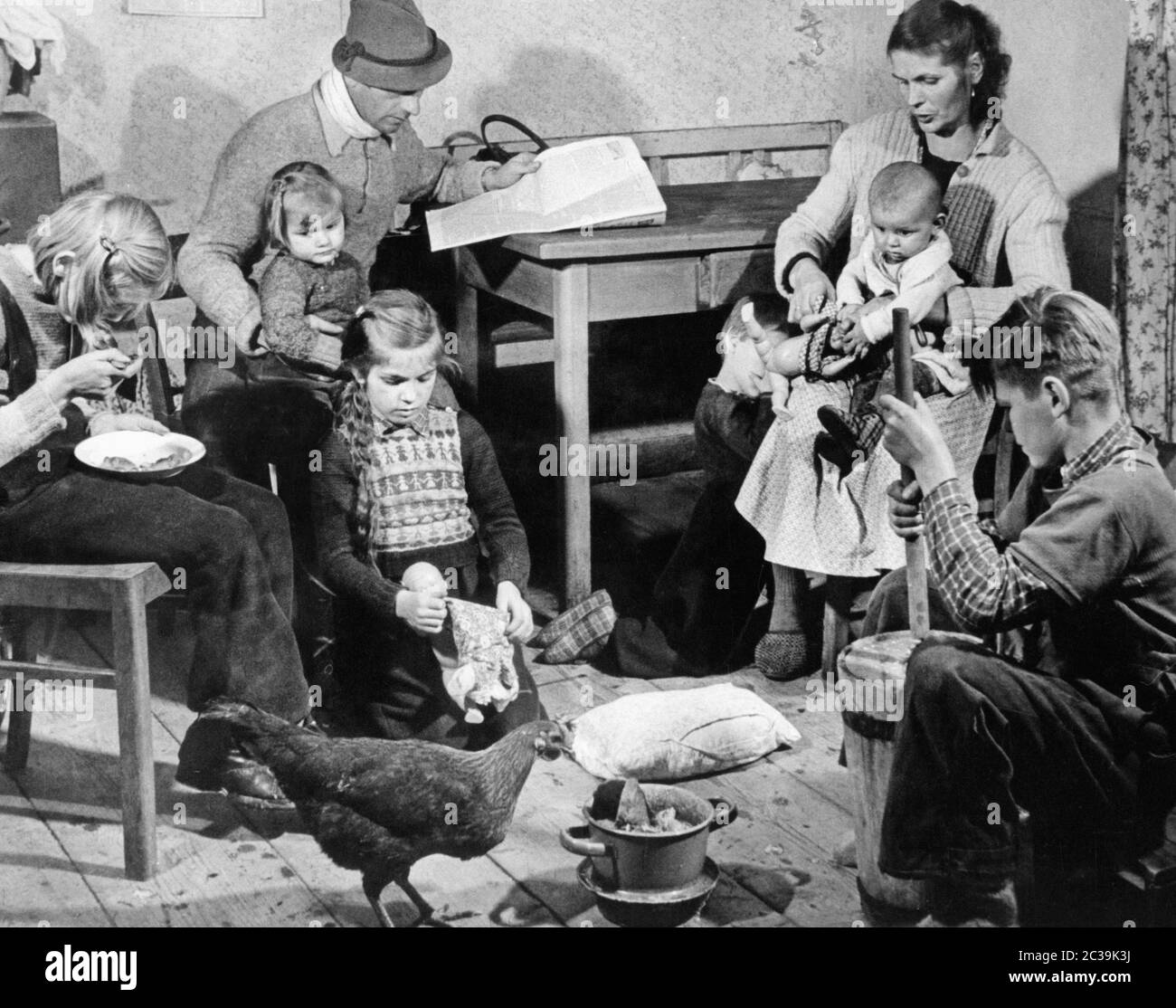 Une famille de cinq enfants dans un bidonville de la forêt bavaroise. Un poulet coule dans la chambre. Une des filles mange quelque chose, une autre joue avec une poupée et le garçon beurres du lait. Banque D'Images