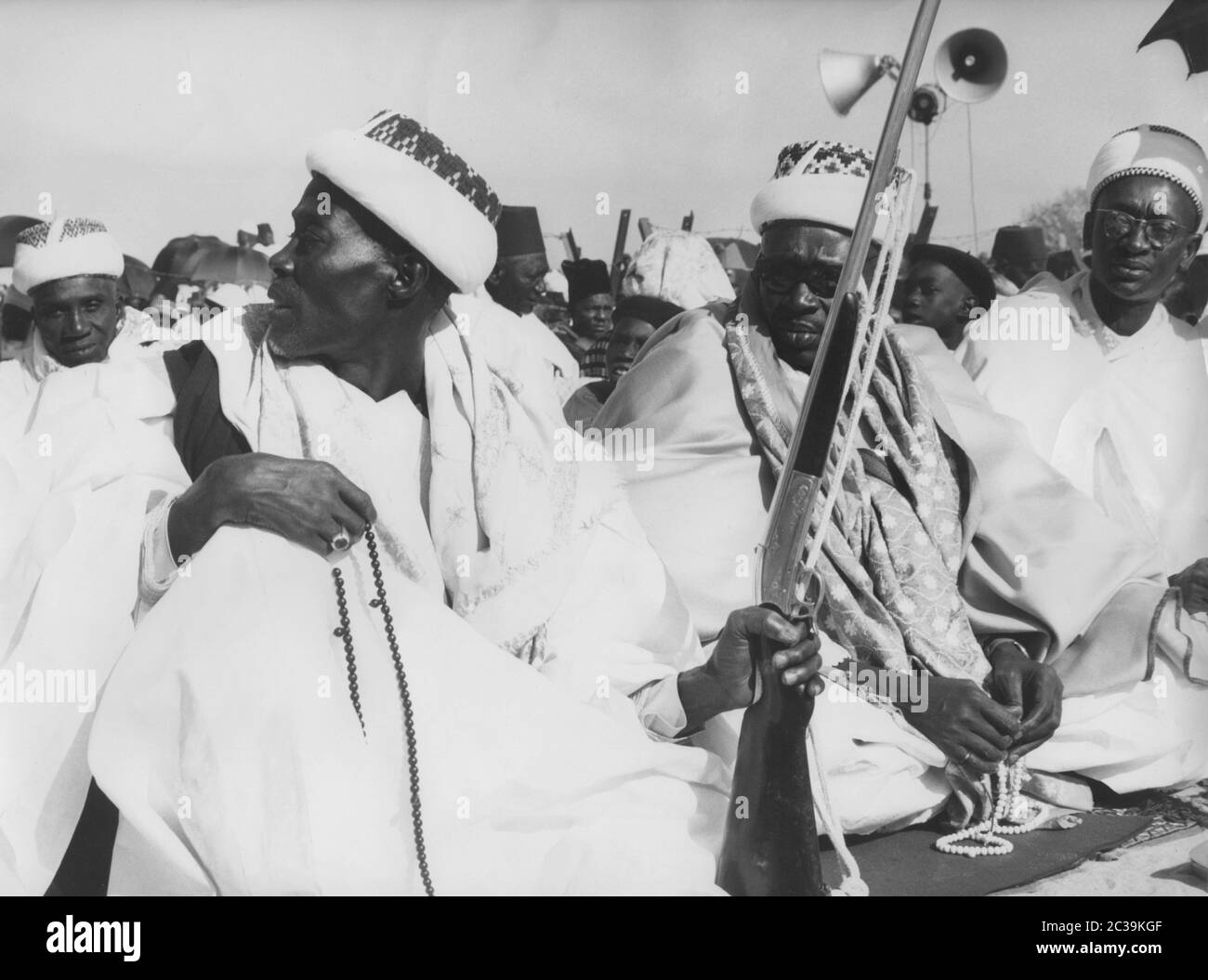 Des hommes musulmans s'assoient sur des tapis de prière au festival du Ramadan à Medina, un quartier de Dakar. Un homme tient un fusil. Les autres hommes tiennent des chaînes de prière. Banque D'Images