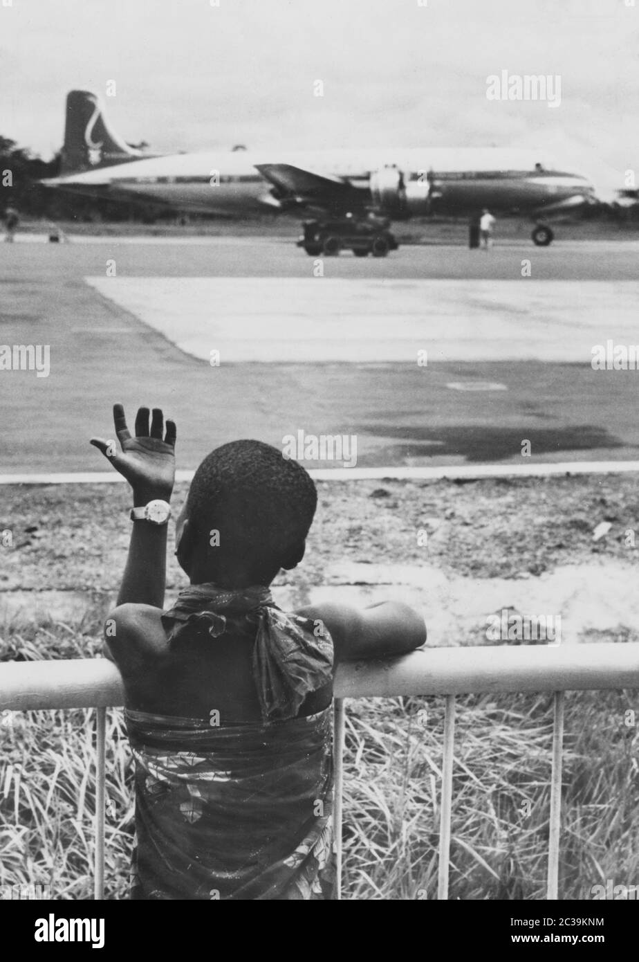 Un enfant se tient à la clôture d'un aéroport et regarde le tablier. En arrière-plan, un avion DC-6 Douglas est en préparation. Banque D'Images