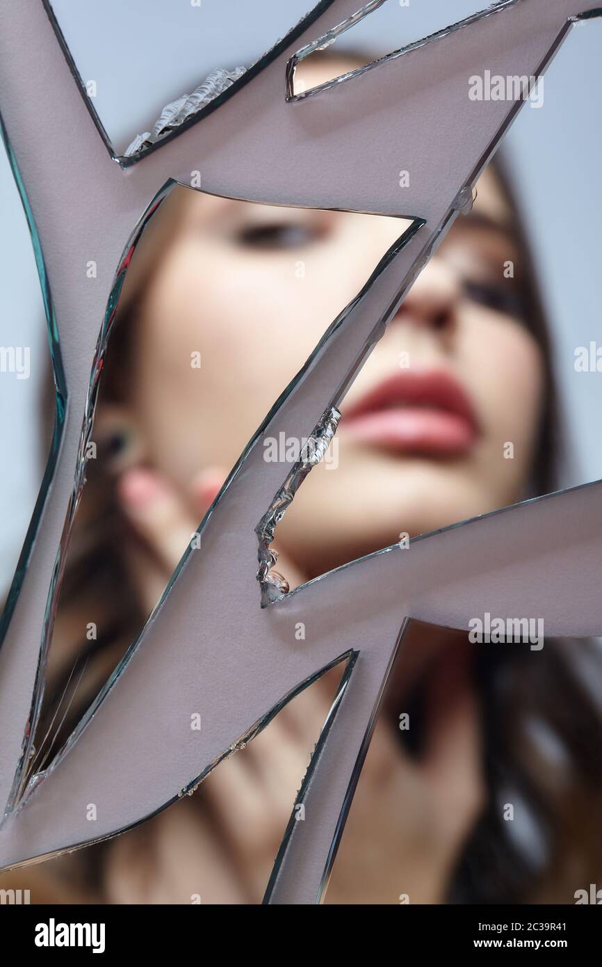 Une jeune femme regarde dans un miroir cassé. Portrait de la femme dans le miroir hors foyer Banque D'Images