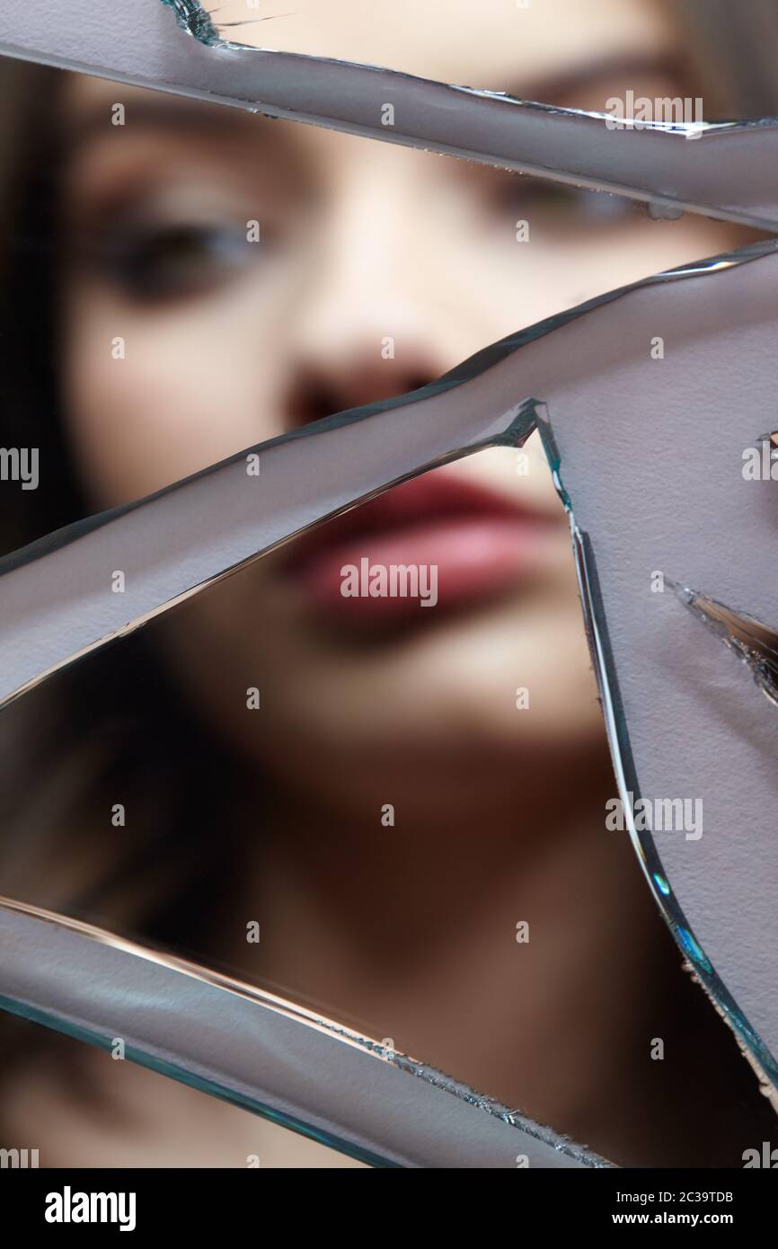 Une jeune femme regarde dans un miroir cassé. Portrait de la femme dans le miroir hors foyer Banque D'Images