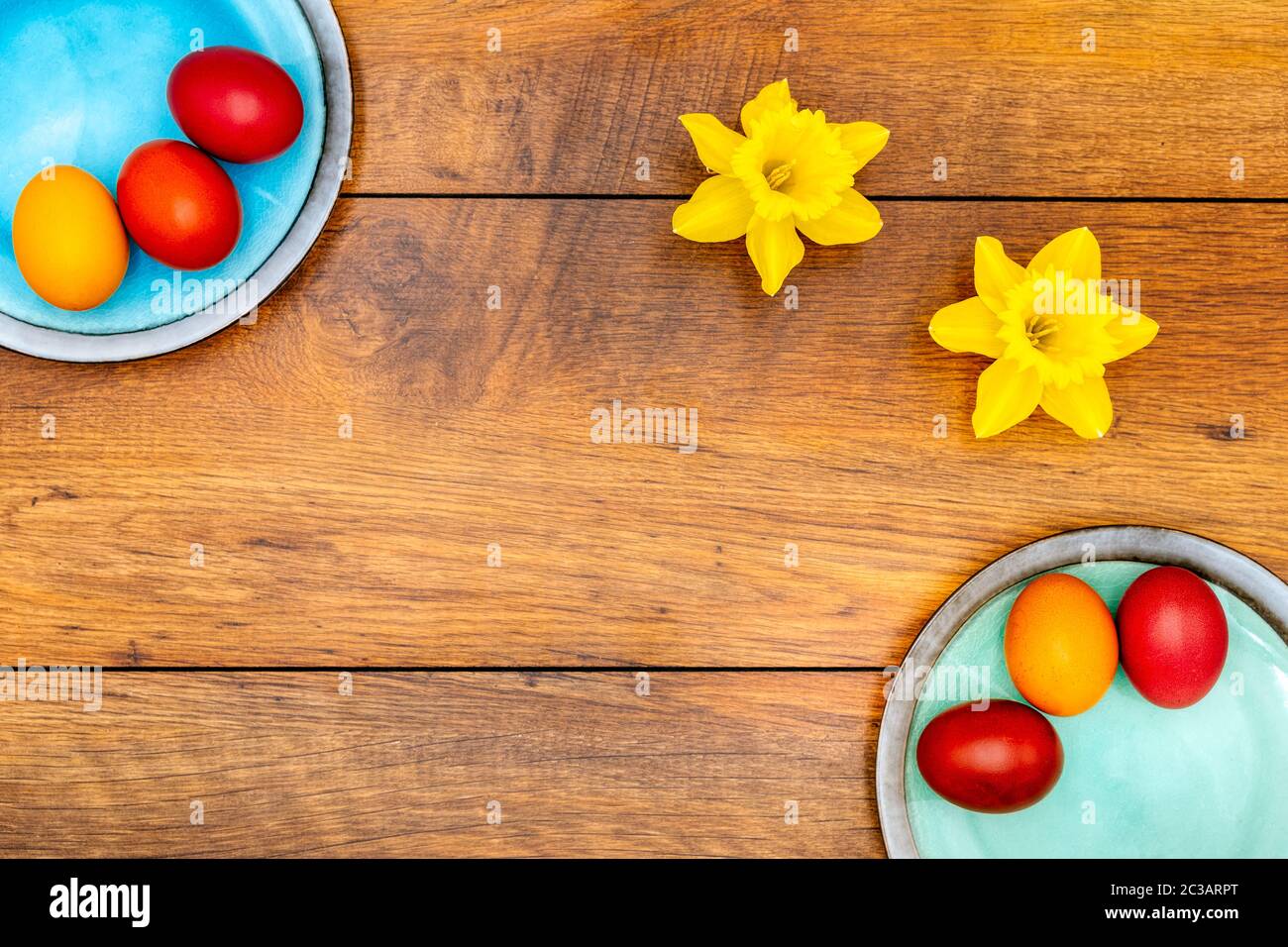 Six œufs de Pâques colorés sur deux assiettes aux couleurs pastel et deux jonquilles sur fond de chêne ancien reconqué, vue du dessus Banque D'Images