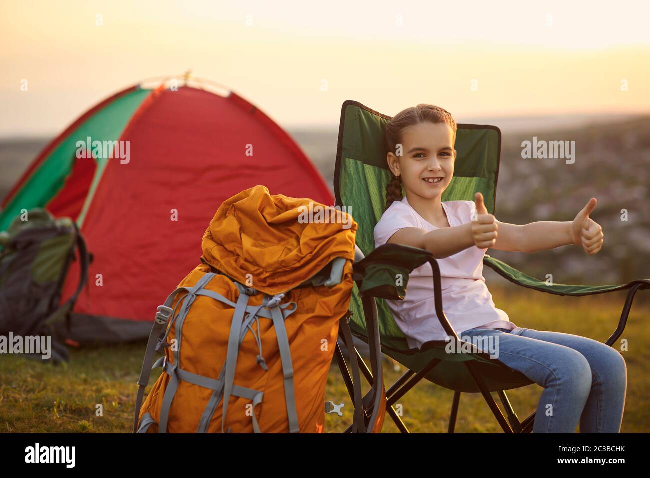Petite fille mignonne montrant le geste des pouces pendant le voyage de camping en montagne. Enfant en vacances d'été Banque D'Images
