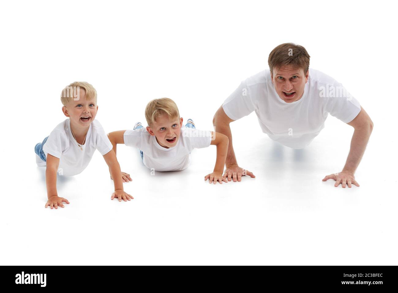 Père avec deux fils. Un jeune homme avec des enfants isolés sur un fond blanc fait des exercices de gymnastique. Pompes. Parentalité, concept de santé l Banque D'Images