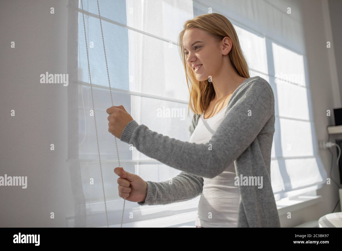 Jolie jeune femme la descente des stores/stores dans son appartement intérieur moderne Banque D'Images