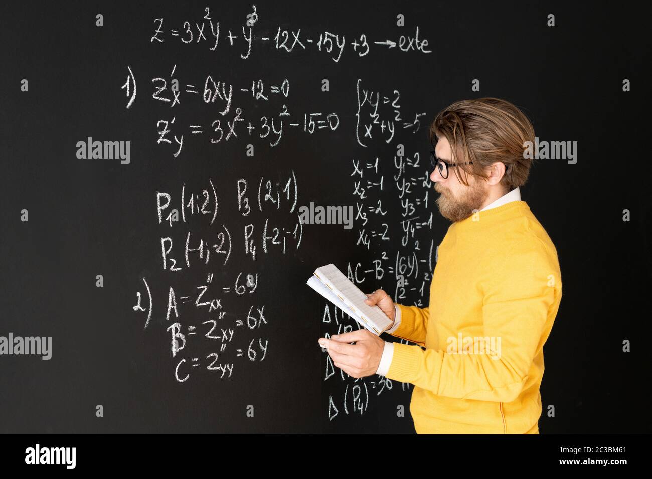Professeur barbu en vêtements décontractés réécrivant des formules sur le tableau noir de son copybook avant de donner la tâche à son public en ligne Banque D'Images