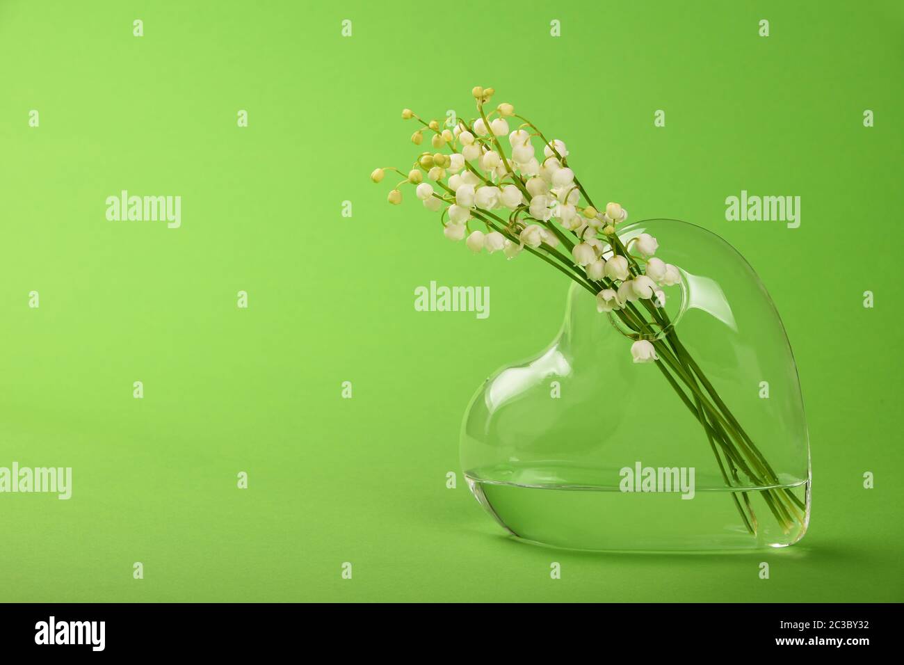 Close up bouquet de lis de la vallée des fleurs de printemps en verre transparent en forme de coeur sur fond vert vase with copy space, low angle vi Banque D'Images