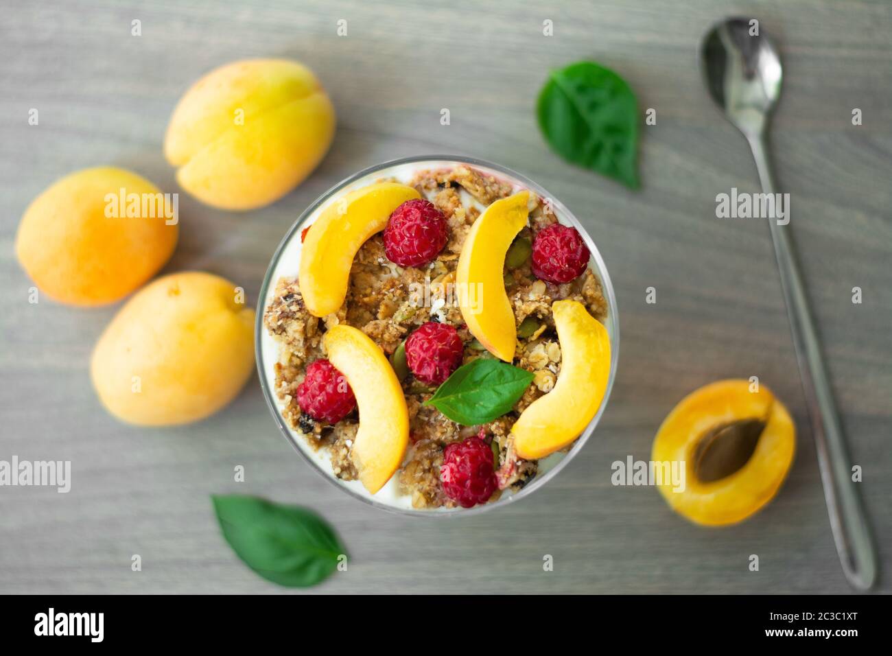 Parfait pour la santé avec yaourt grec, granola maison, tranches d'abricot et framboises dans un gobelet en verre. Fond en bois gris avec abricots Banque D'Images