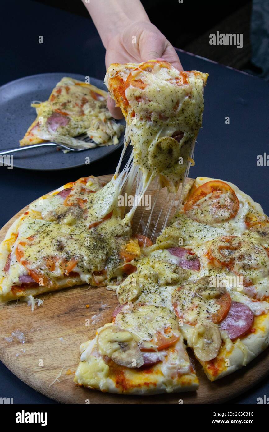 A woman's hand prend un morceau de pizza avec une planche en bois qui se dresse sur un beau fond noir, dans l'arrière-plan est une assiette avec un morceau de p Banque D'Images