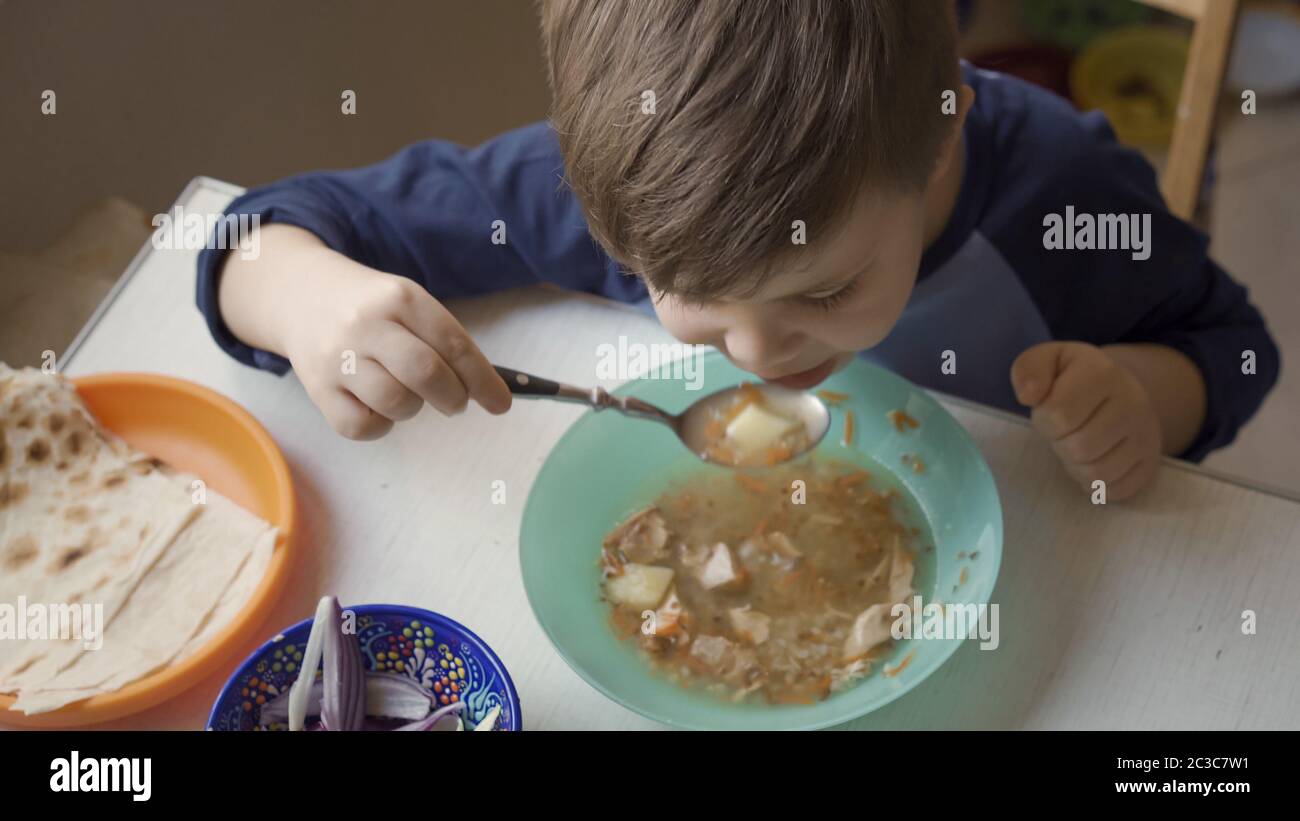 Un enfant d'âge préscolaire mignon apprend à manger seul. Un garçon affamé tient une grande cuillère à manger de la soupe seule à table. Vue grand angle Banque D'Images