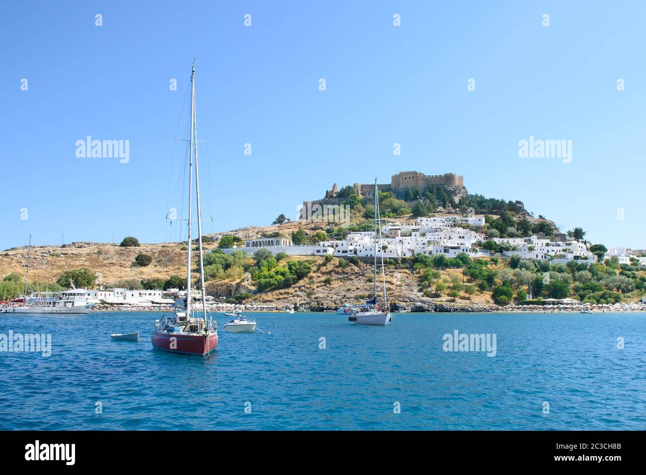 Bateaux à voile ancrés dans la baie, juste sous le village de Lindos avec l'Acropole sur la colline (Rhodes, Grèce) Banque D'Images