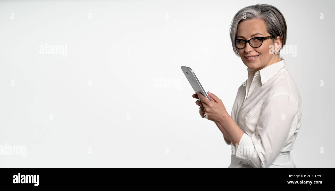 Une femme d'affaires joyeuse travaille sur une tablette numérique sur fond blanc. Femme d'âge mûr en blanc regardant l'appareil photo. Blanc horizontal avec spase vide pendant Banque D'Images