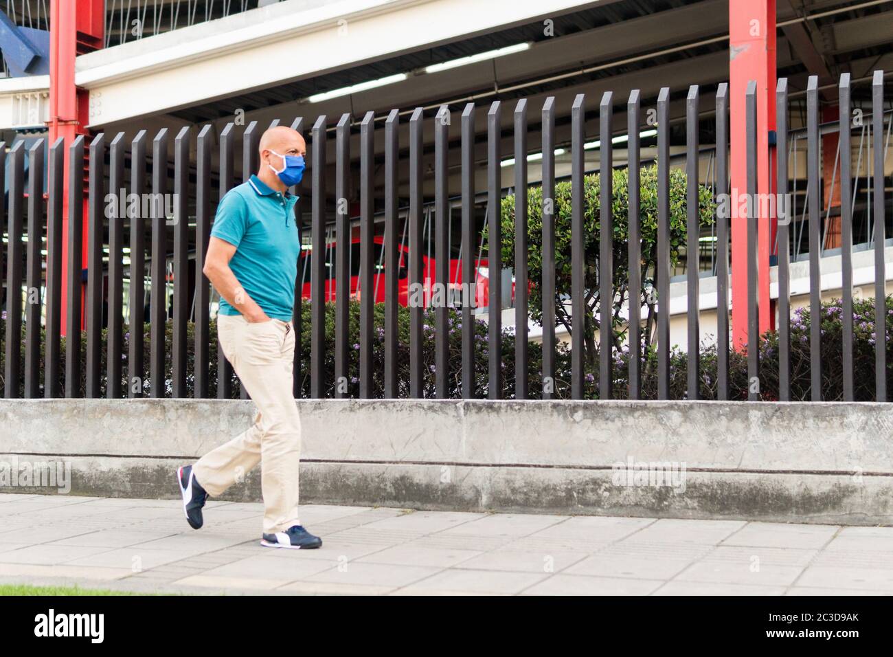 Homme latin d'âge moyen portant un masque pour éviter la propagation du coronavirus ; marchant dans la rue de Bogota. Colombie. Parking à l'arrière. Chemise bleue Banque D'Images