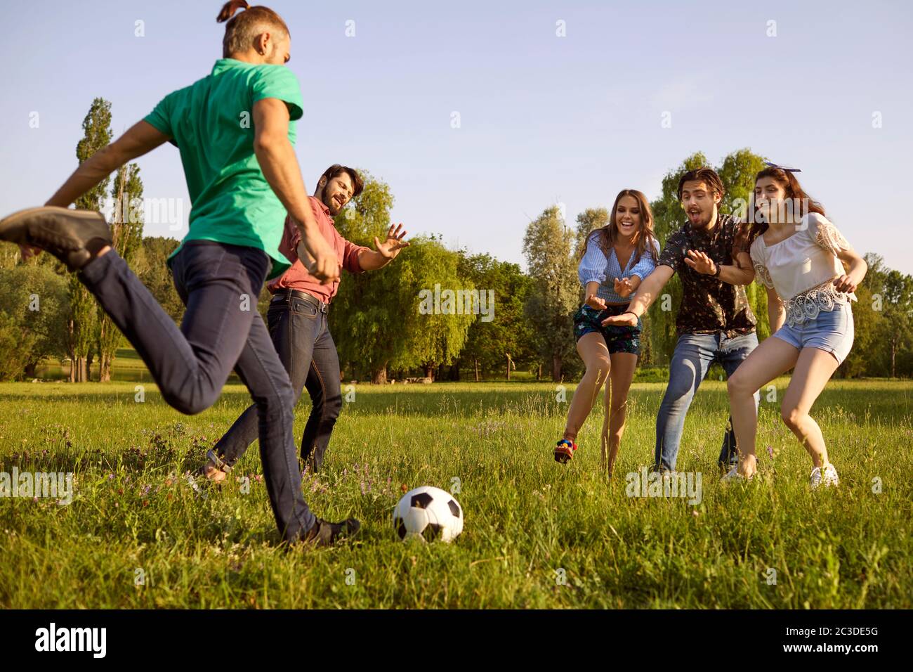 Jeunes amis jouant au football sur un pré vert. Les étudiants s'amusent le week-end d'été dans la nature Banque D'Images