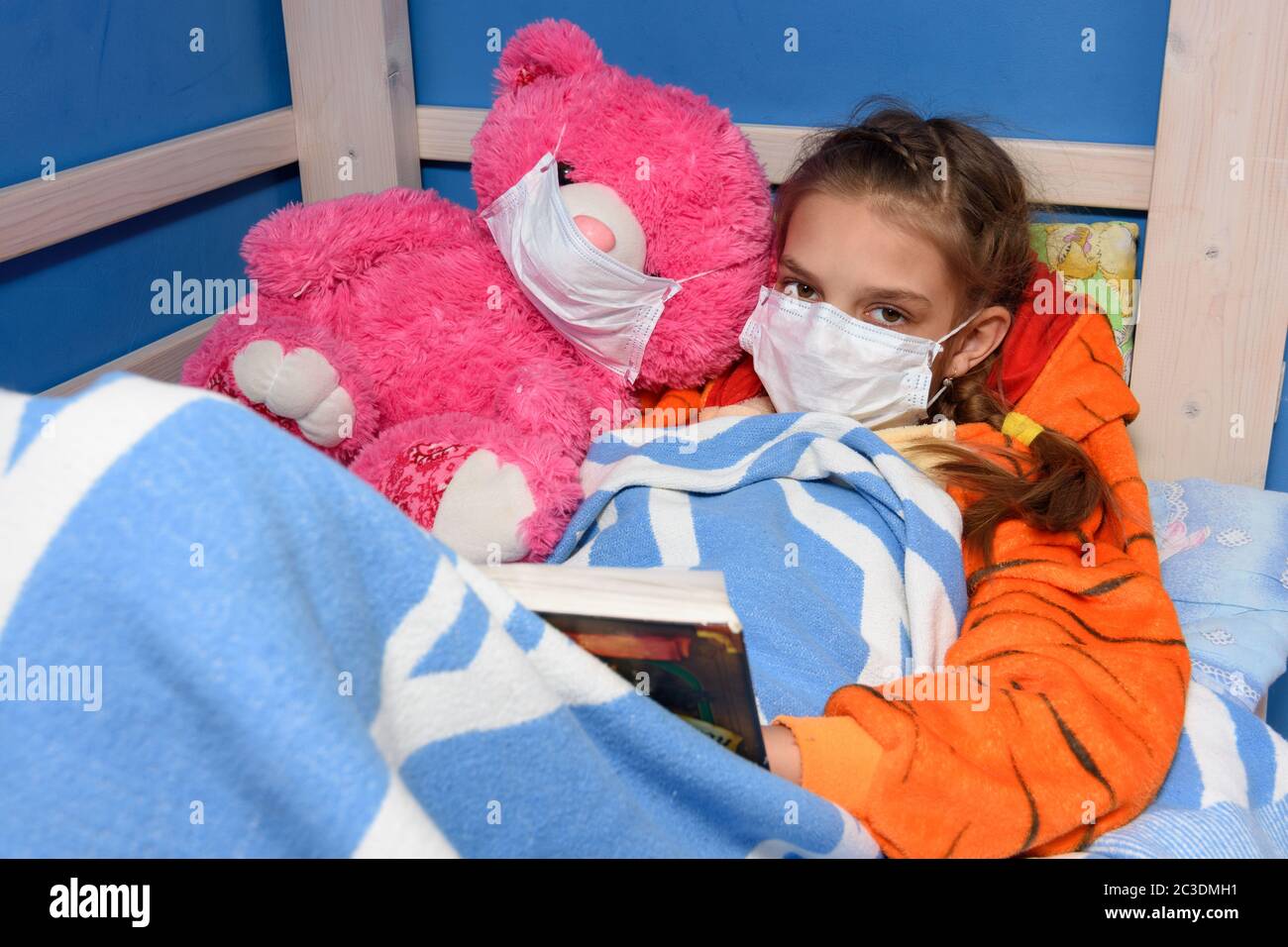 Fille et jouet en peluche dans les masques médicaux dans le lit lire un livre, et regardé dans le cadre Banque D'Images