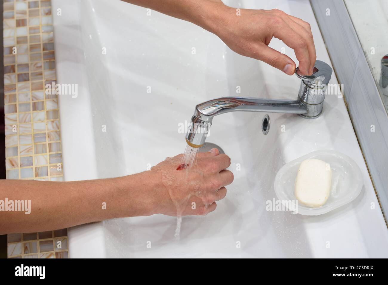 Un homme lave une blessure sur sa main sous un ruisseau d'eau dans le lavabo Banque D'Images