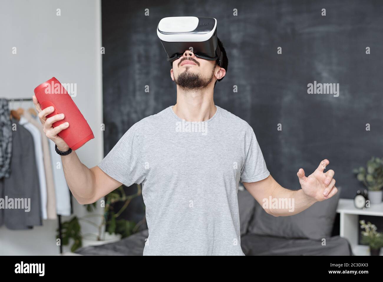 Jeune homme en VR lunettes tenant un haut-parleur portable tout en explorant le monde virtuel dans le jeu vidéo Banque D'Images