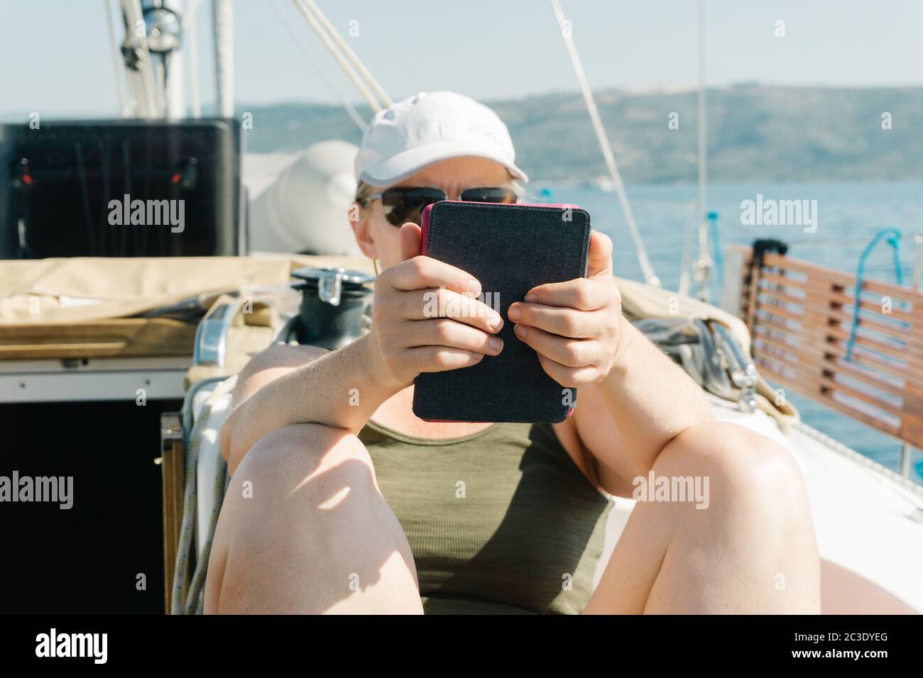Femme assise sur le pont d'un yacht appréciant la lecture dans son ebook. Concept de voyage et de vacances. Banque D'Images