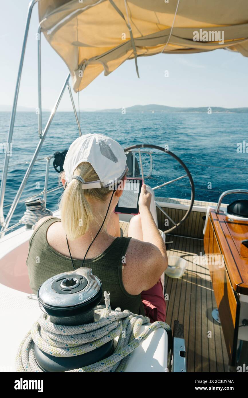 Femme assise sur le pont d'un yacht appréciant la lecture dans son ebook. Concept de voyage et de vacances. Banque D'Images