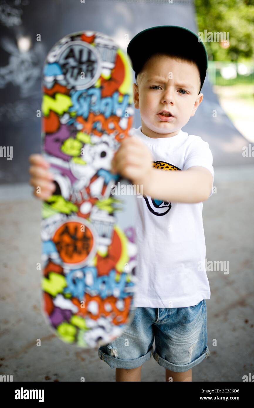 Garçon avec un skate dans un parc de skate. Un garçon avec des lunettes apprend à skate. Banque D'Images