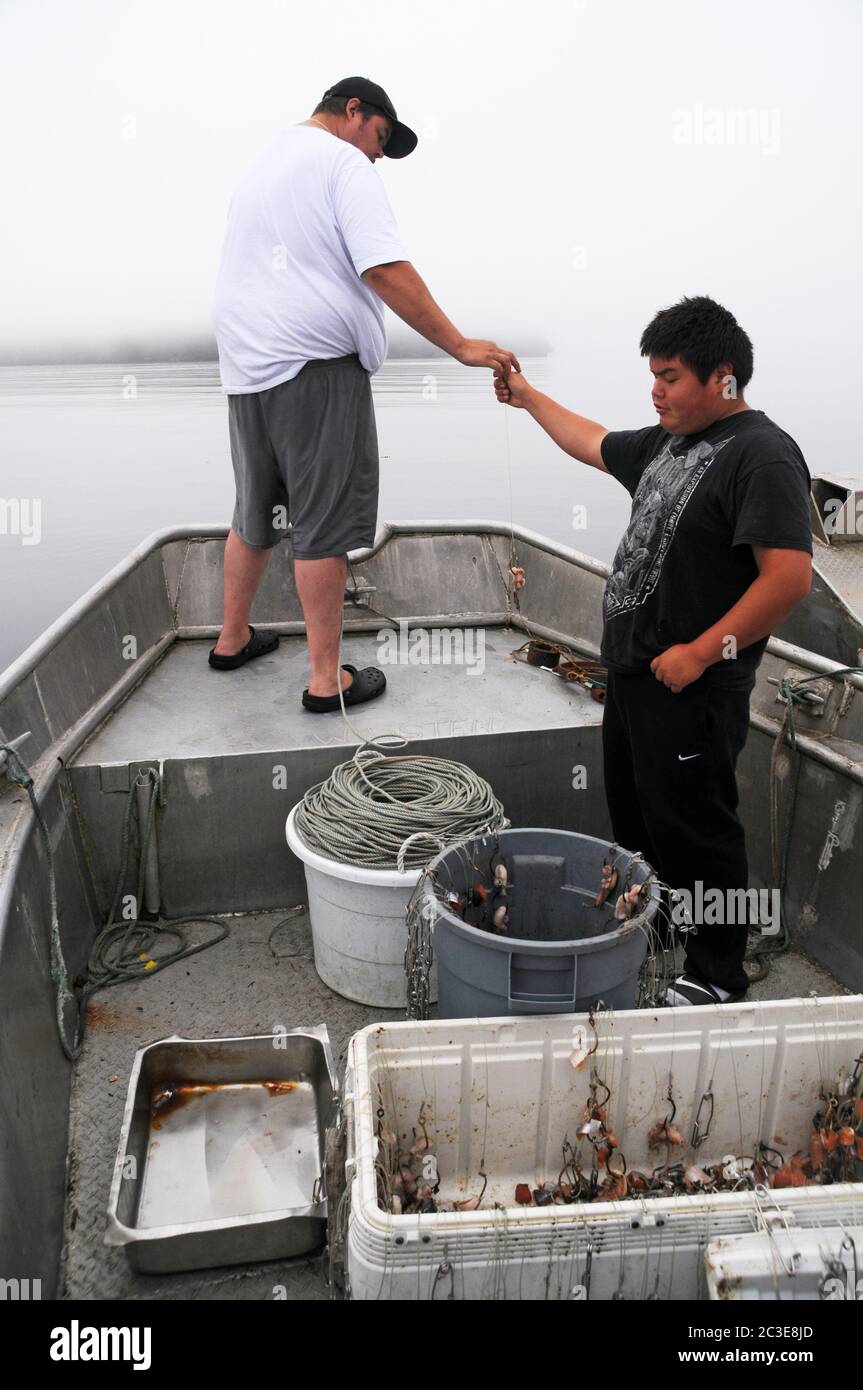 Deux hommes autochtones des Premières nations qui appâts une ligne de pêche à longue ligne dans le Pacifique, dans la forêt pluviale de Great Bear, Bella Bella, Colombie-Britannique, Canada. Banque D'Images