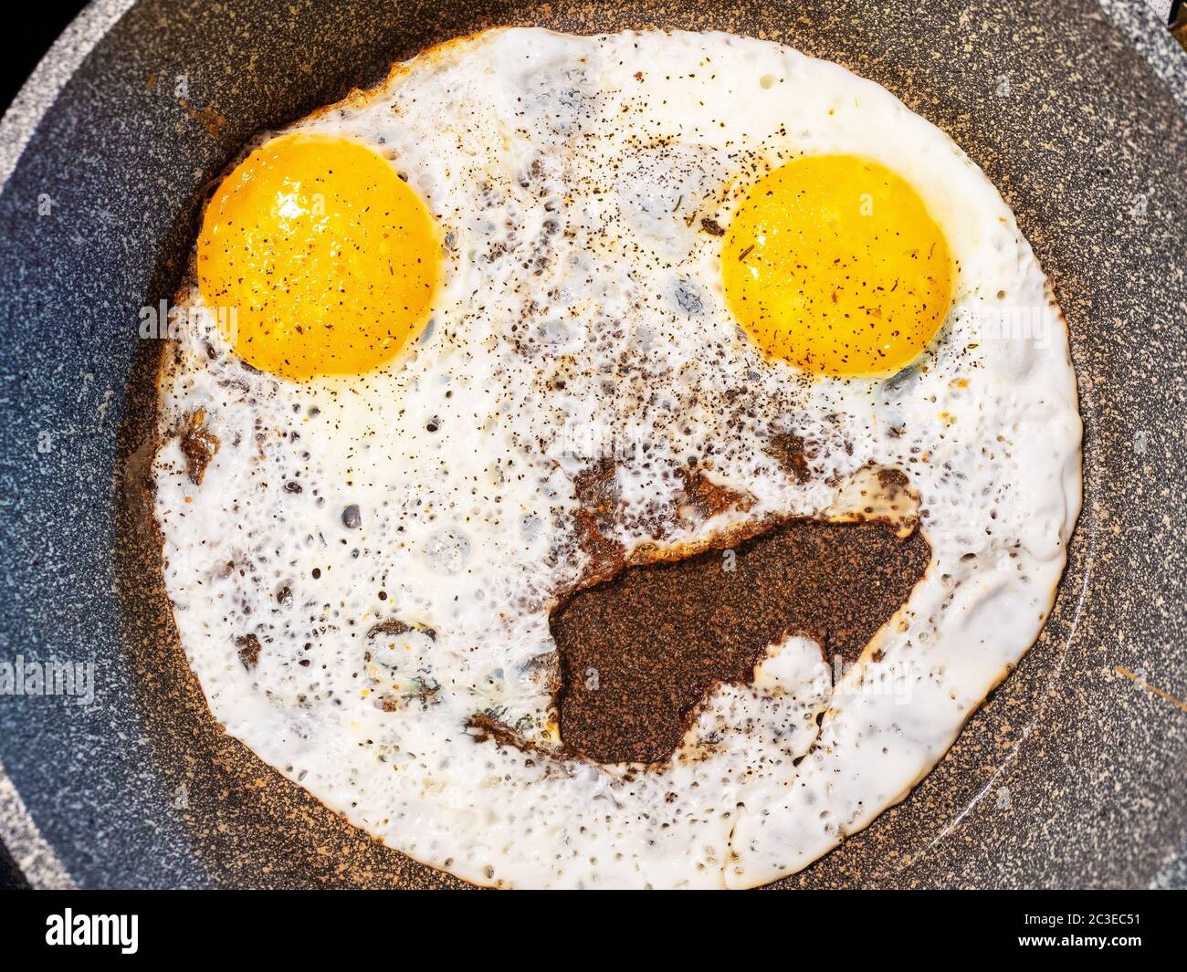 Photo d'œufs brouillés inhabituels de près, ressemblant à un visage souriant dans une poêle grise Banque D'Images