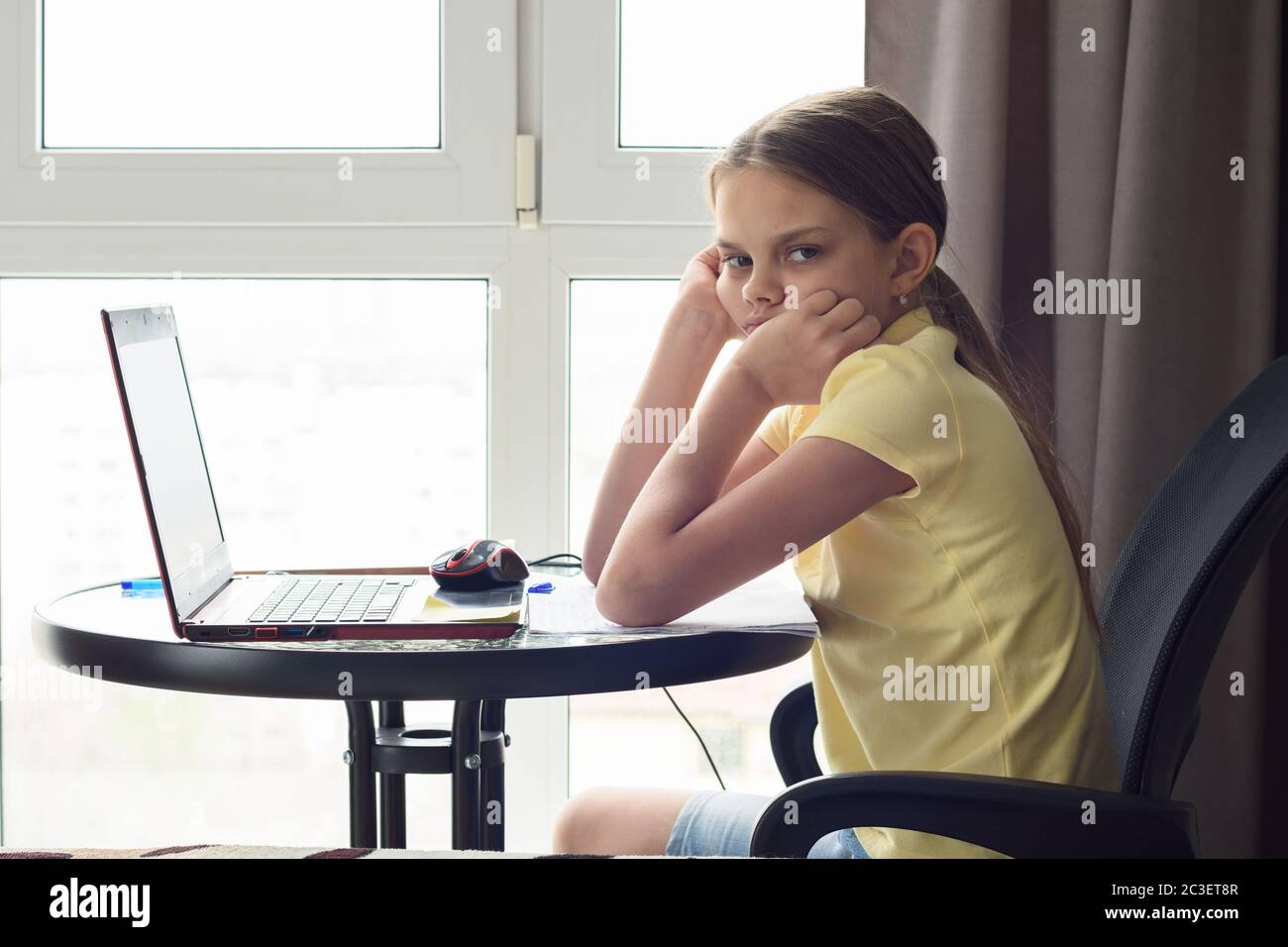Une jeune fille bouleversée est assise à une table à la maison, fait des devoirs et regarde avec mécontentement Banque D'Images