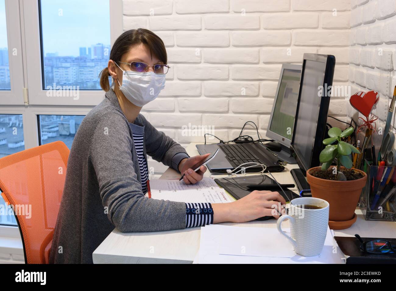 Une jeune fille malade dans un masque médical en auto-isolation fonctionne à distance, regarda dans le cadre Banque D'Images