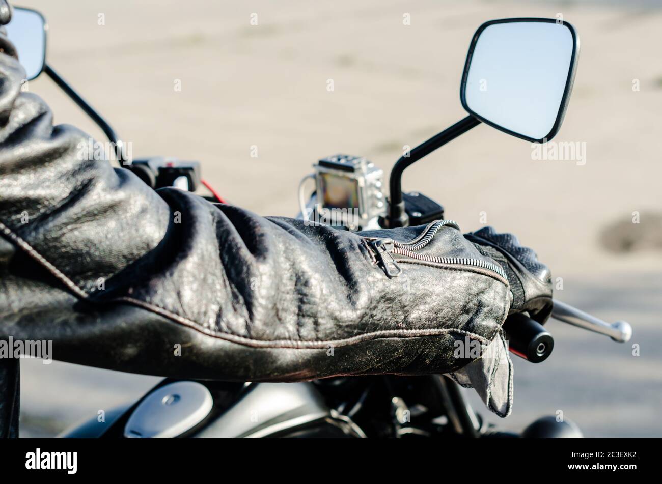 Mains d'un motard dans une veste en cuir noire et des gants sur le guidon d'une moto Banque D'Images