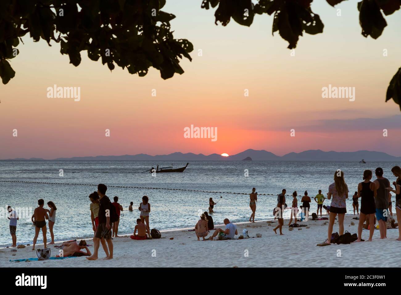 Province de Krabi, Thaïlande - 14 février 2019 : beaucoup de touristes sur la plage de Phra nang profitent de la vue sur le coucher du soleil dans la mer. Sur fond de montagnes, un bateau en bois navigue sur la mer. Banque D'Images