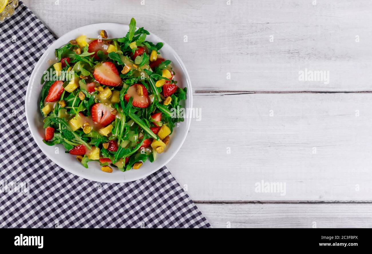 Salade verte avec des arugula fraîches, des fraises et des pistaches sur fond de bois blanc. Banque D'Images
