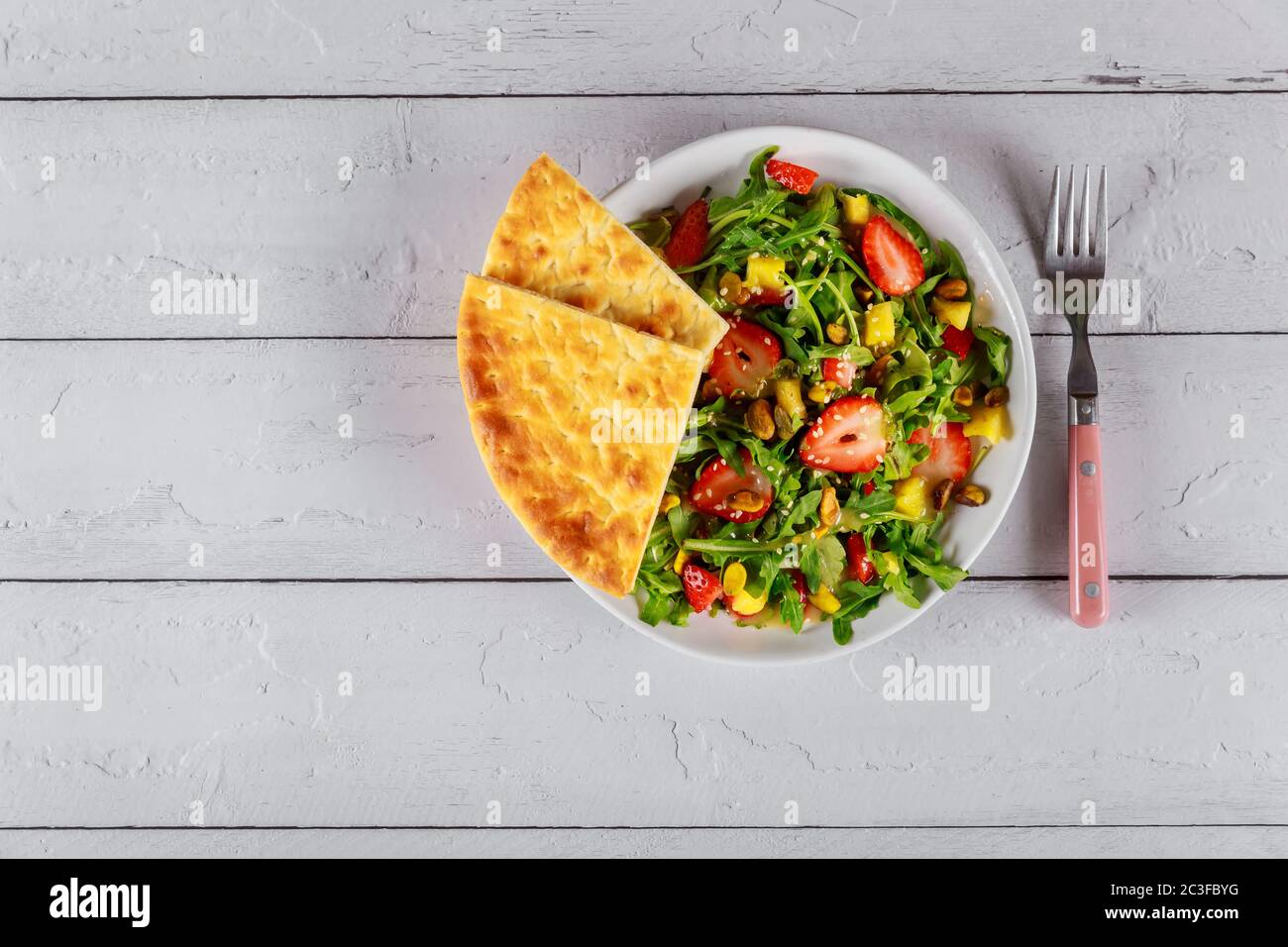 Salade fraîche avec fraises, arugula, ananas et pistaches sur table en bois blanc. Banque D'Images