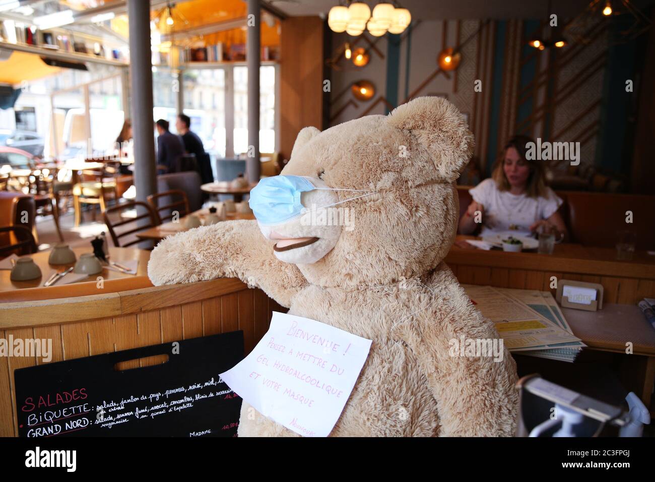 Pékin, France. 18 juin 2020. Un ours en peluche portant un masque affiche  un panneau indiquant « Bienvenue! N'oubliez pas votre masque et votre gel  hydro dans un restaurant à Paris, France,