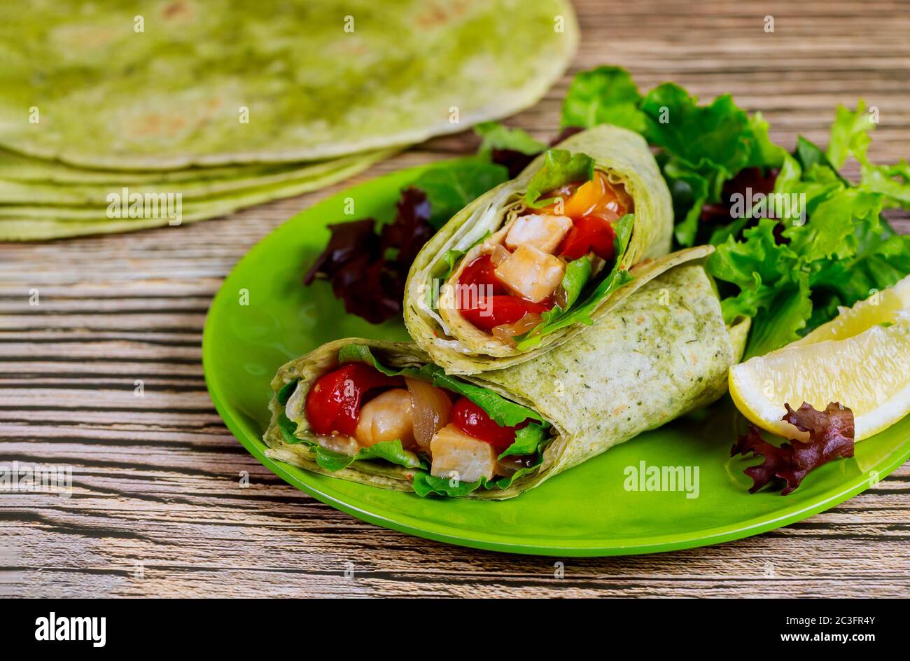 Envelopper avec du poulet grillé et des légumes sur l'assiette avec de la salade verte et du citron sur une table en bois. Banque D'Images