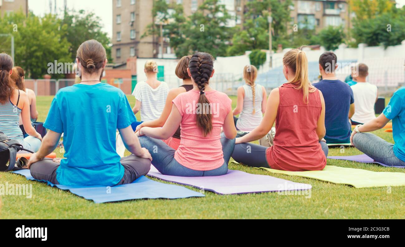 Yoga groupe de jeunes filles et les hommes médite assis dans le parc Banque D'Images