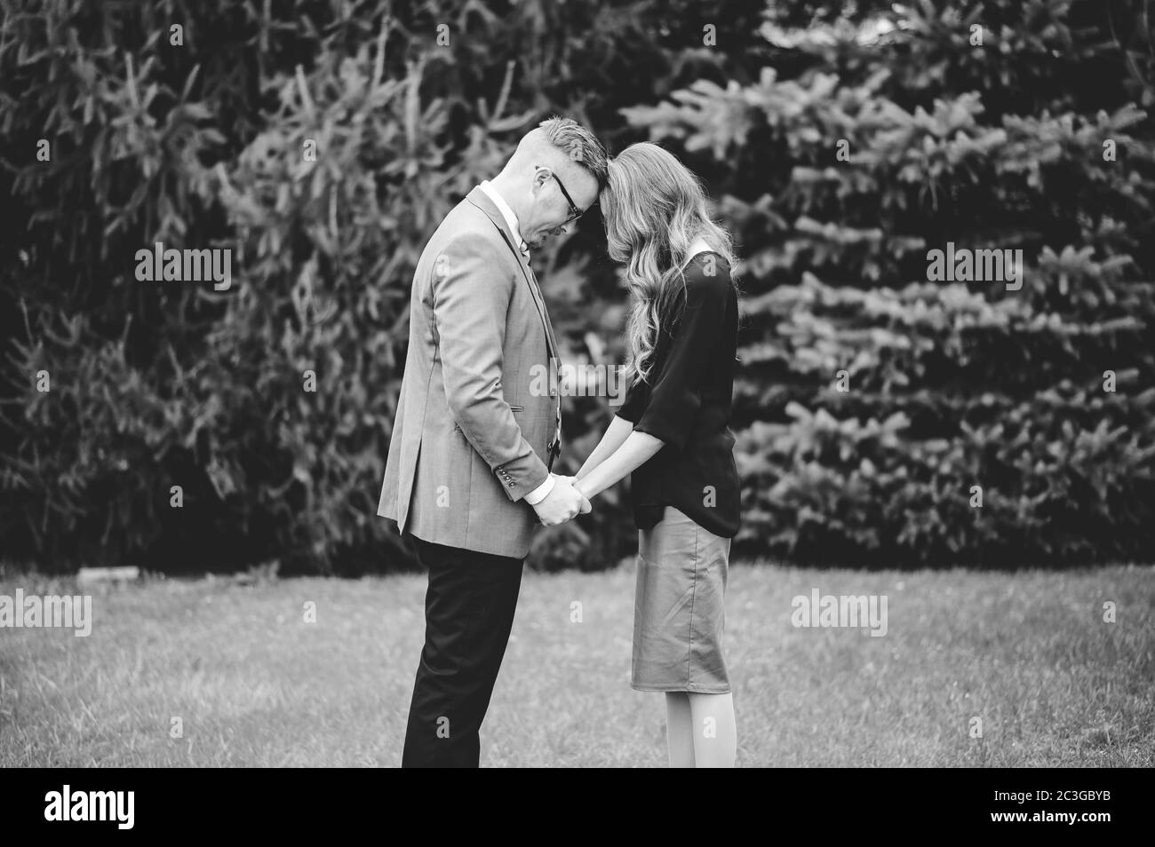 Prise de vue en niveaux de gris d'un couple tenant les mains de chacun autre et prier dans un jardin Banque D'Images