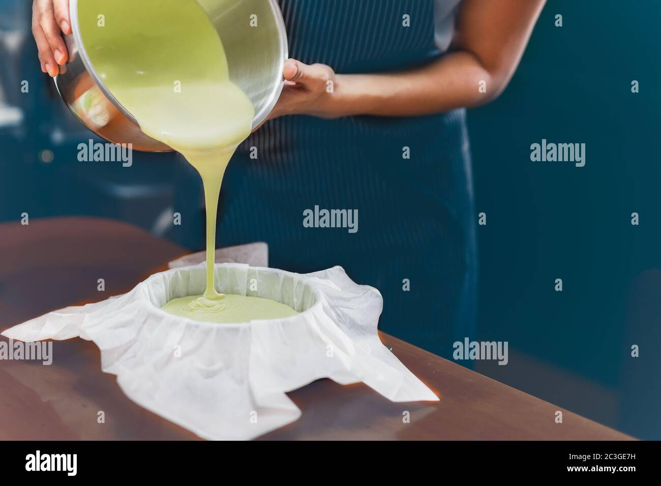 Femme versant de la pâte de thé vert matcha dans un moule rembourré de papier parchemin. Banque D'Images