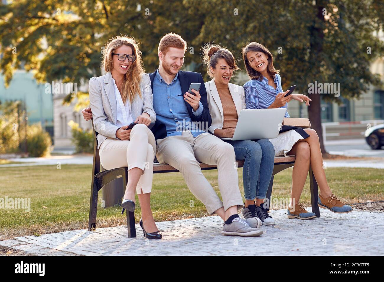 les jeunes gens d'affaires du caucase rient au parc assis sur un banc avec leur téléphone portable, ordinateur portable, tablette. concept de pause de bonne humeur en extérieur Banque D'Images