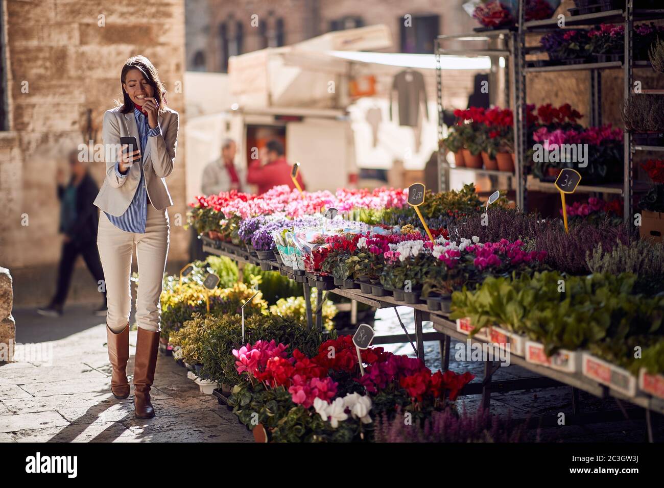 Belle jeune femme marchant devant la boutique de fleurs en Italie, Toscana, regardant son téléphone cellulaire avec un sourire Banque D'Images