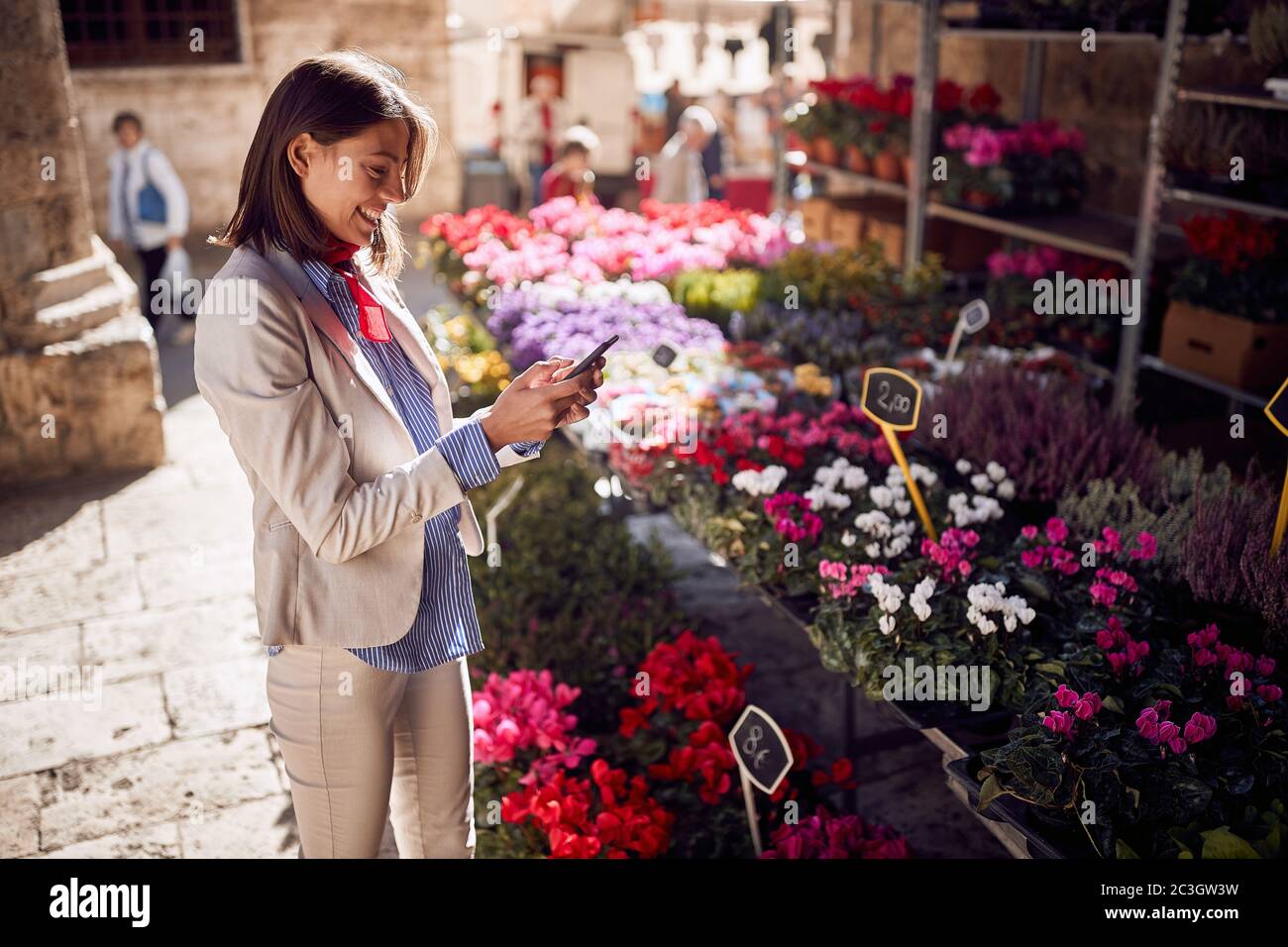 Belle jeune femme textant sur son téléphone cellulaire, souriant, devant la boutique de fleurs, Italie, Toscane Banque D'Images