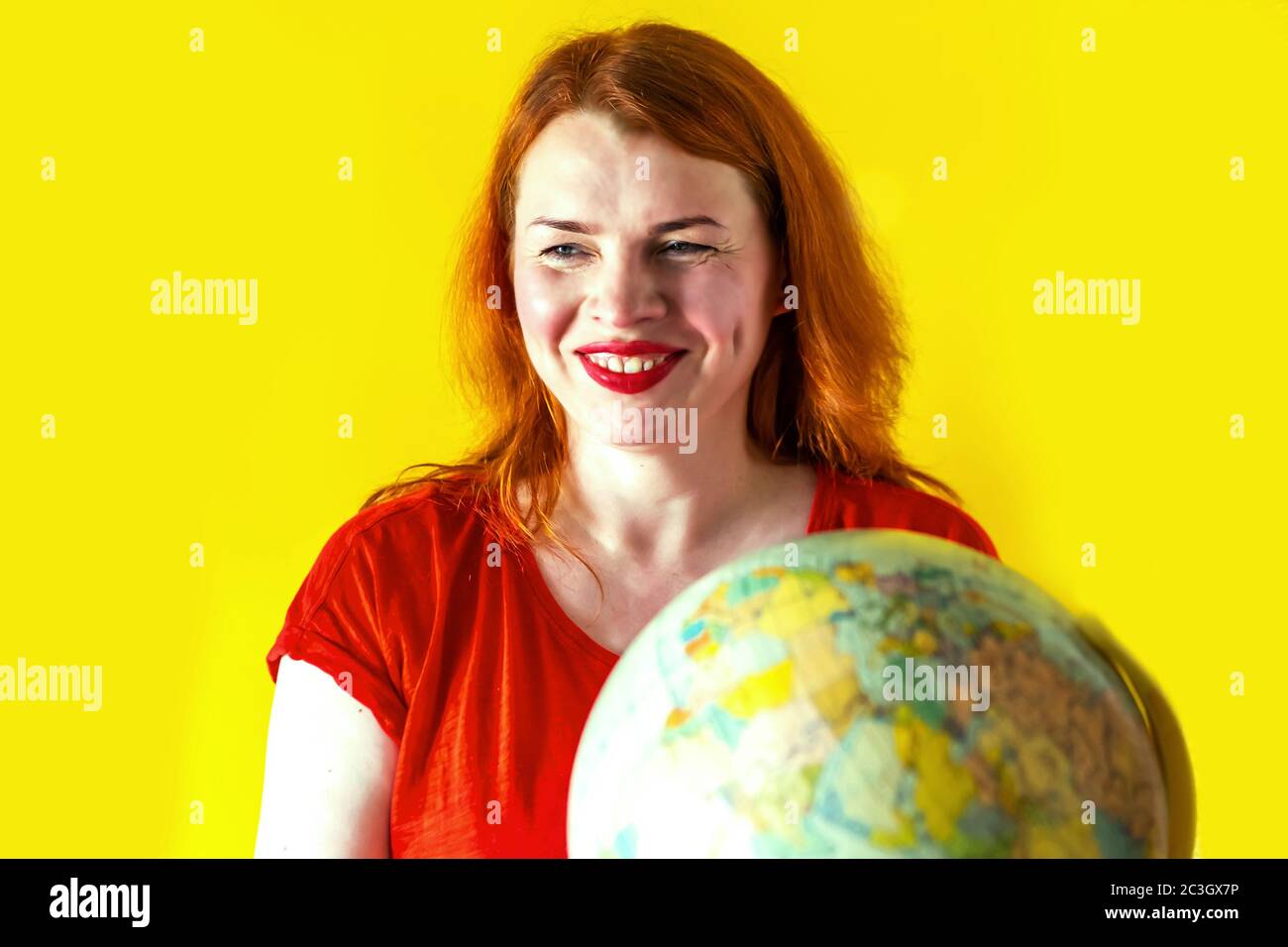 Portrait de la belle fille à tête rouge avec globe dans les mains sur fond jaune. Concept de voyage Banque D'Images