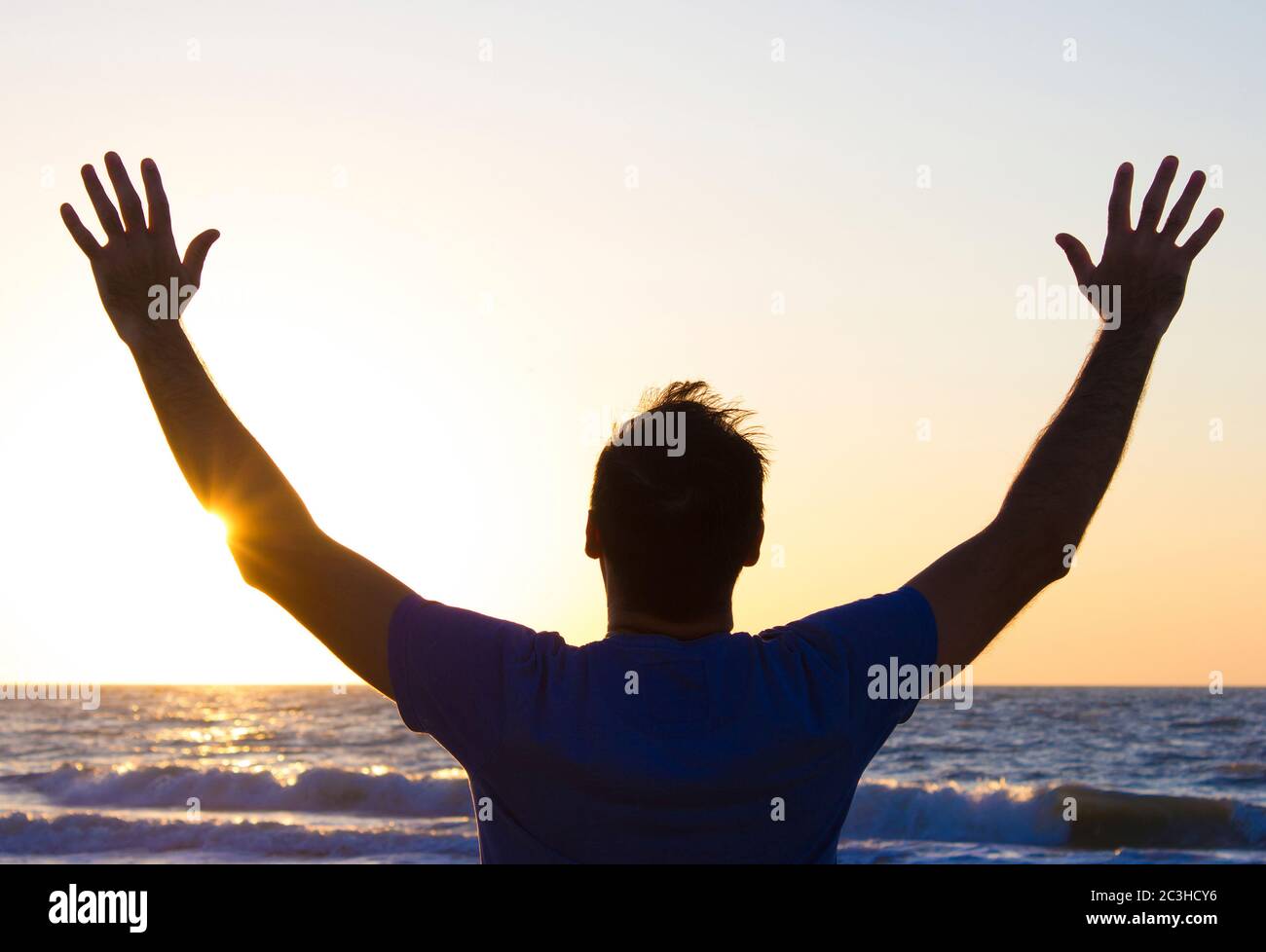 Jeune homme avec les mains au lever du soleil sur un fond de ciel bleu et de mer, horizon plage aube Banque D'Images