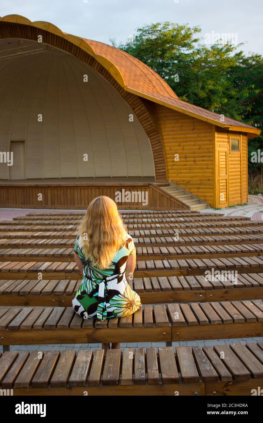 La fille est assise seule dans son dos parmi les nombreux bancs du théâtre de rue Banque D'Images