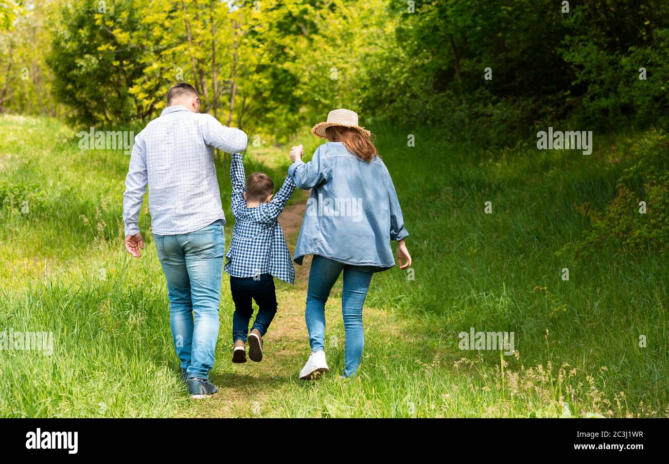 Vue arrière des jeunes parents à pied avec leur enfant à la campagne, espace copie Banque D'Images