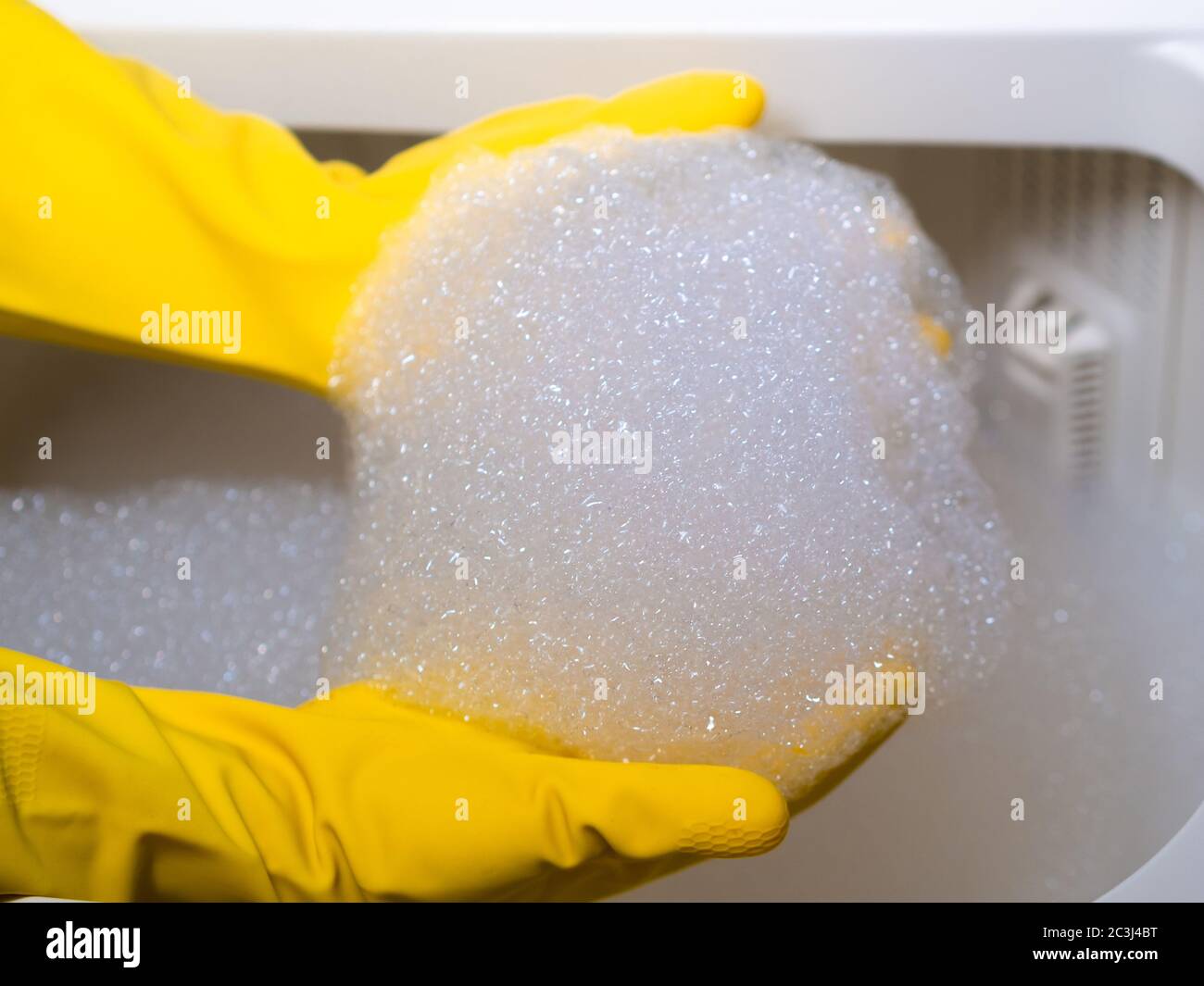 mains d'une jeune fille avec des gants jaunes nettoyage avec de la mousse d'un lave-linge Banque D'Images