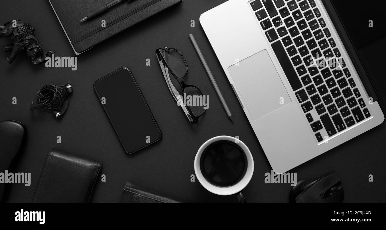 Concept de bureau professionnel. Combinaison de fournitures de bureau et de gadgets sur fond de table noir. Avec ordinateur portable, téléphone portable, lunettes, ordinateur portable, tasse de café. Banque D'Images