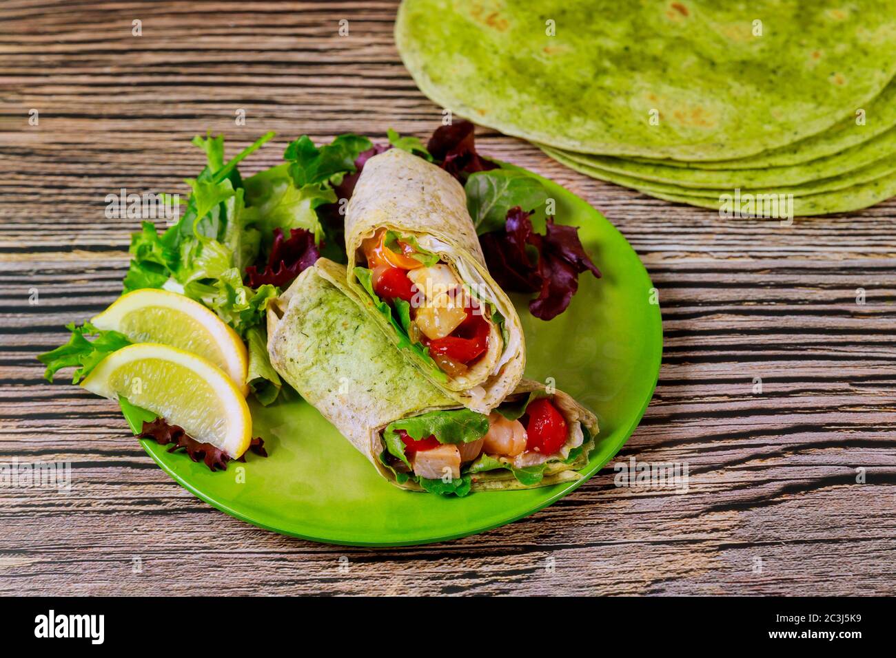 Envelopper avec du poulet grillé et des légumes sur l'assiette avec de la salade verte et du citron sur une table en bois. Banque D'Images